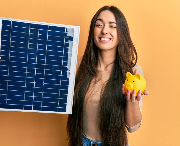 Young hispanic girl holding photovoltaic solar panel and piggy bank winking looking at the camera with sexy expression, cheerful and happy face. Young hispanic girl holding photovoltaic solar panel and piggy bank winking looking at the camera with sexy expression, cheerful and happy face.